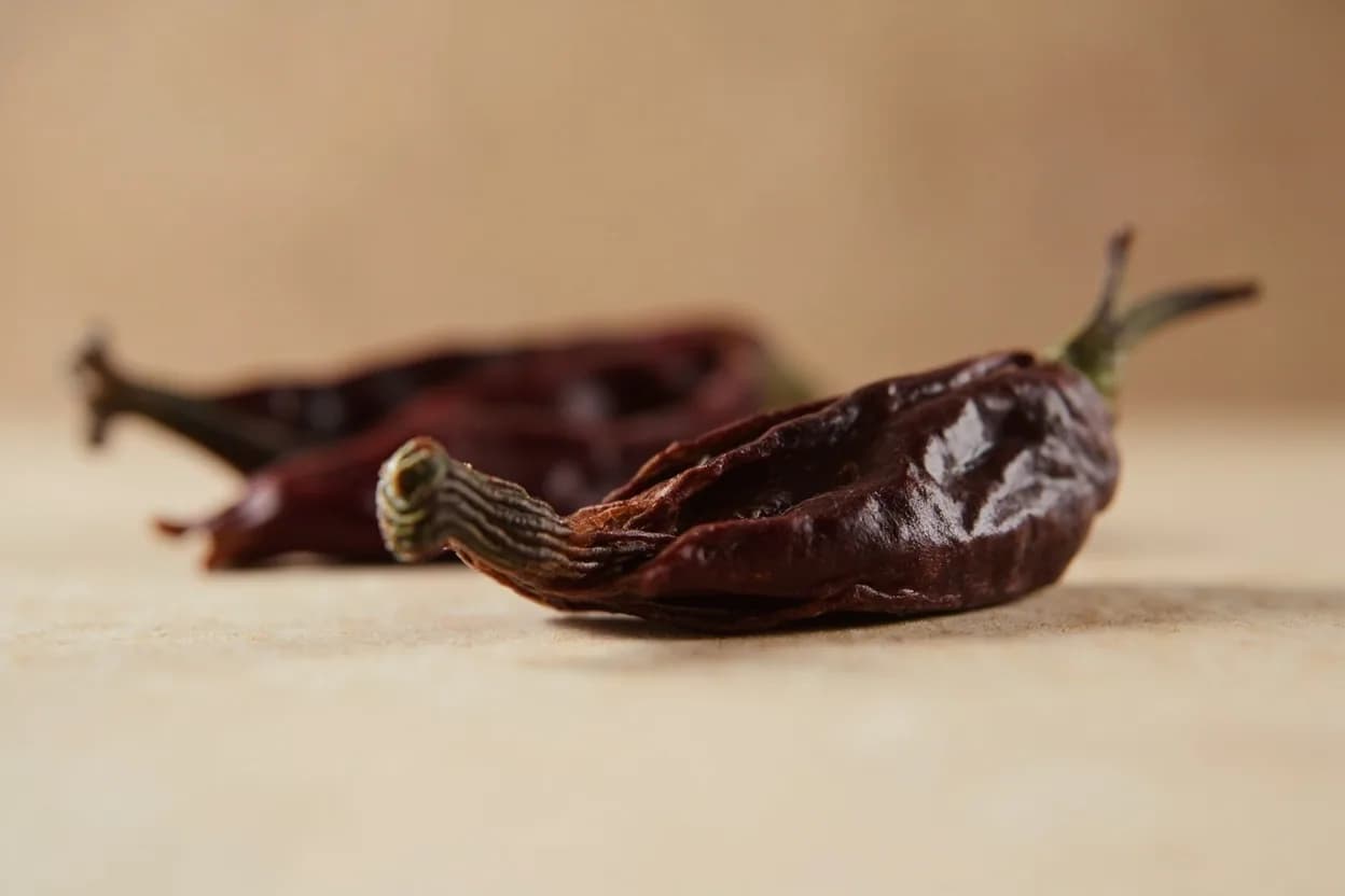 Ancho Chile in its natural form. The ancho is simply the poblano pepper (Capsicum annuum) in its dried state — wrinkled, mahogany-black, and flat, the name coming from the Spanish for 'wide. Tasting profile: dark chocolate, dried plum and raisin, tobacco leaf, mild earthiness.