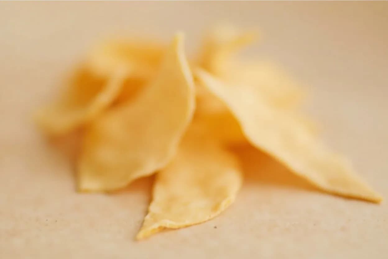 Feuilletine in its natural form. Feuilletine (pailleté feuilletine) is a confectionery ingredient made from very thin, lacy crêpe batter that is baked until it caramelizes and crisps, then broken into irregular flakes. Tasting profile: light caramel sweetness, baked grain, faintly biscuity, neutral, clean butter note, subtle toffee at the edge.