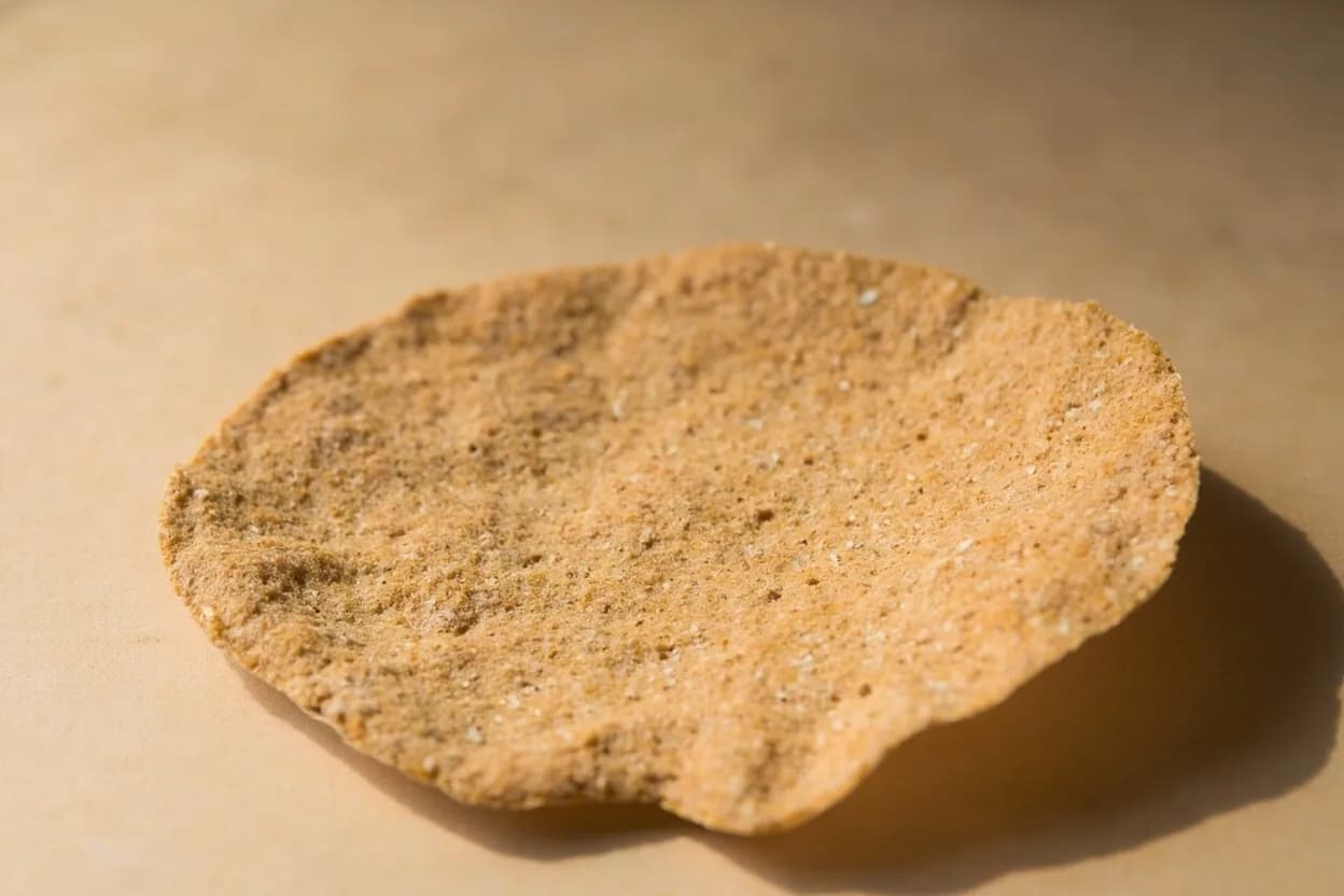 Injera in its natural form. Injera is a large, fermented flatbread made from teff flour batter that is left to ferment for two to three days, then poured onto a hot clay griddle (mitad) in a single pour. Tasting profile: sharp lactic sourness from long fermentation, earthy, molasses-like teff base note, mild iron-mineral undertone, gentle whole-grain bitterness.