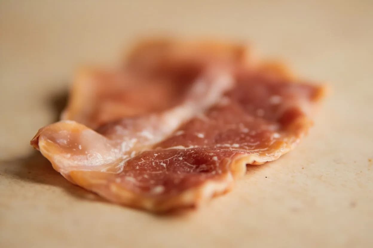 Pancetta in its natural form. Pancetta is an Italian cured pork belly seasoned with salt, black pepper, juniper, nutmeg, and sometimes rosemary, then air-dried for weeks to months. Tasting profile: mild, clean pork fat with subtle sweetness, gentle salt cure without aggressive funk, black pepper and juniper top notes, warm spice underpinning from nutmeg and clove.